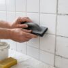 Tiler applying fresh grout during tile regrouting in a bathroom