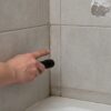 Signs of bathroom waterproofing problems including dark grout and peeling paint near a shower corner